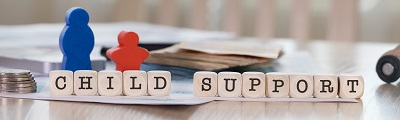 A photo of the words child support in wooden blocks with parent child figurines and coins and papers in the backgound